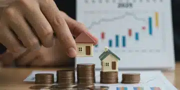 Hand placing model house on coins, symbolizing financial impact of Fed rate hike on housing in 2025.